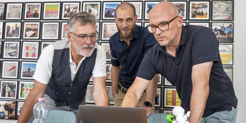 Die drei Gründer des KI Hafen schauen gemeinsam auf einen Laptop im Büro in Zug